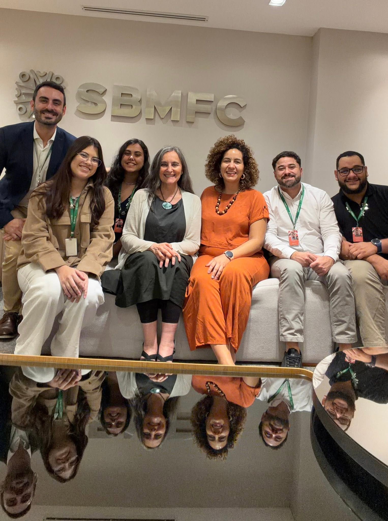 Sete pessoas, incluindo a Prof.ª Viviana Martinez-Bianchi, sentadas sob o letreiro da SBMFC na sede da organização.